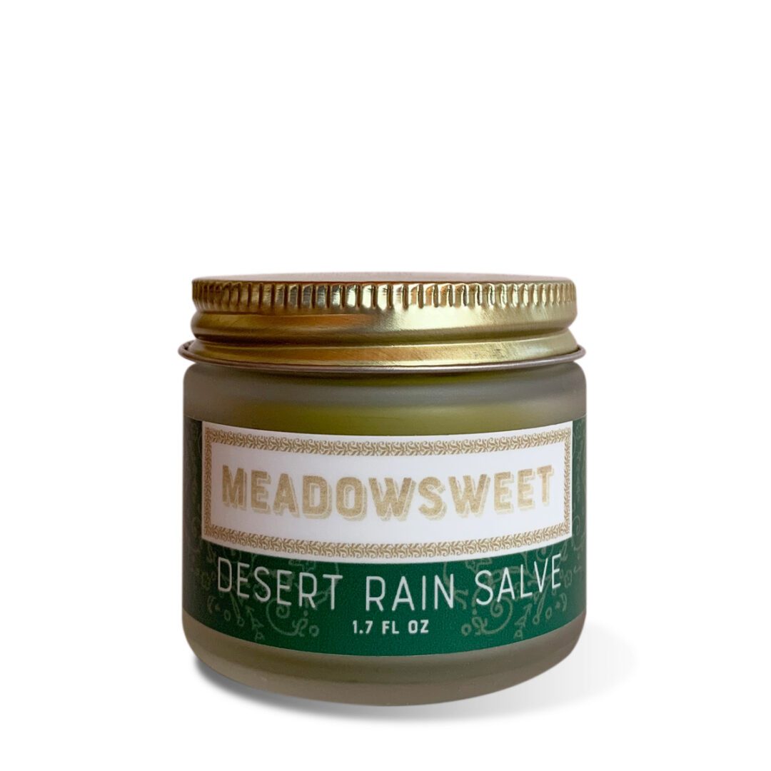 A small glass jar with a gold lid and green and white label containing Desert Rain Salve.