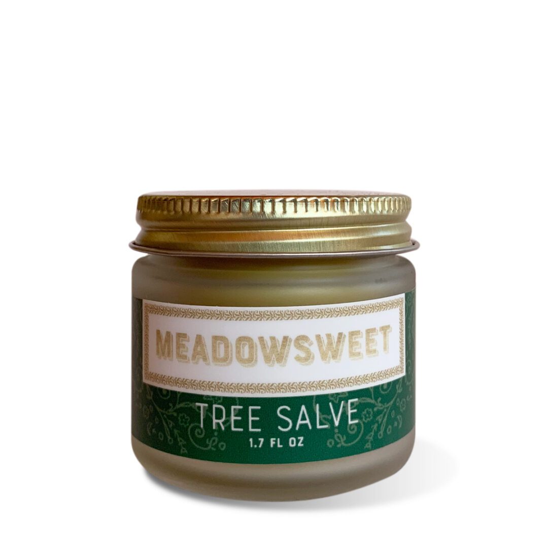 A small frosted glass jar with gold lid and green and white label containing Tree Salve.