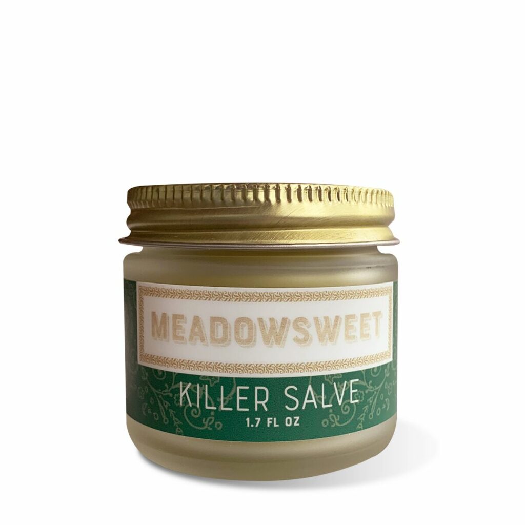 A small frosted glass jar with a gold lid and green and white label containing Killer Salve.