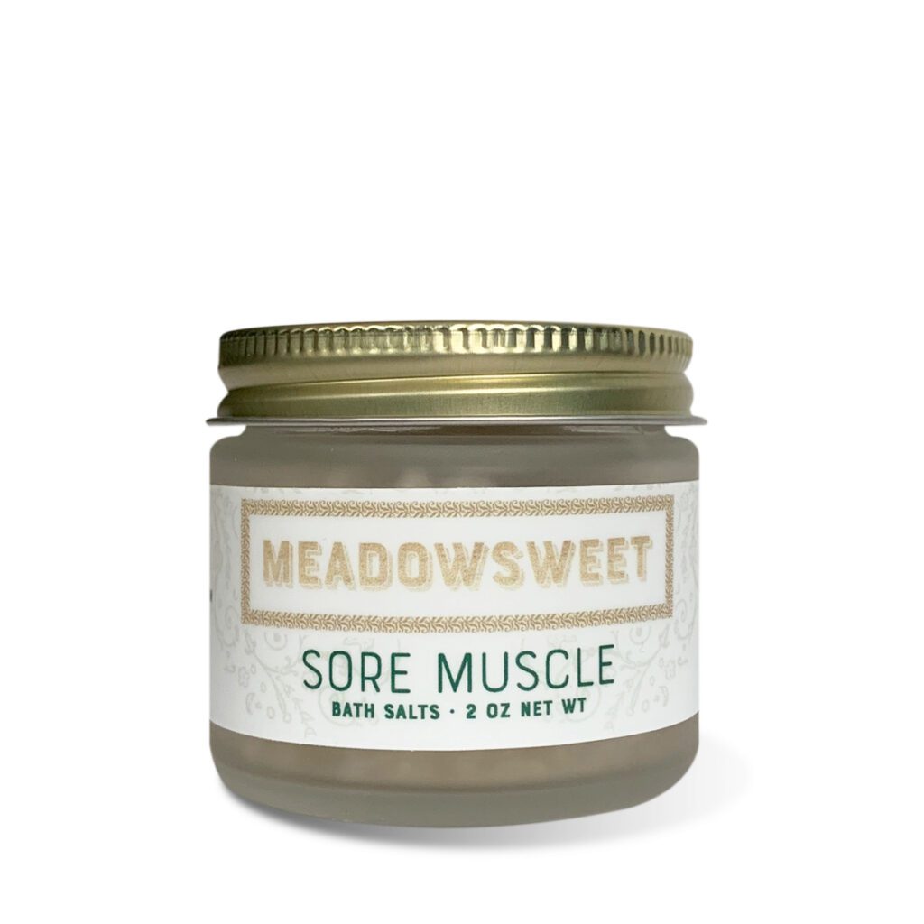 A frosted glass jar with a gold lid containing Sore Muscle Bath Salts.
